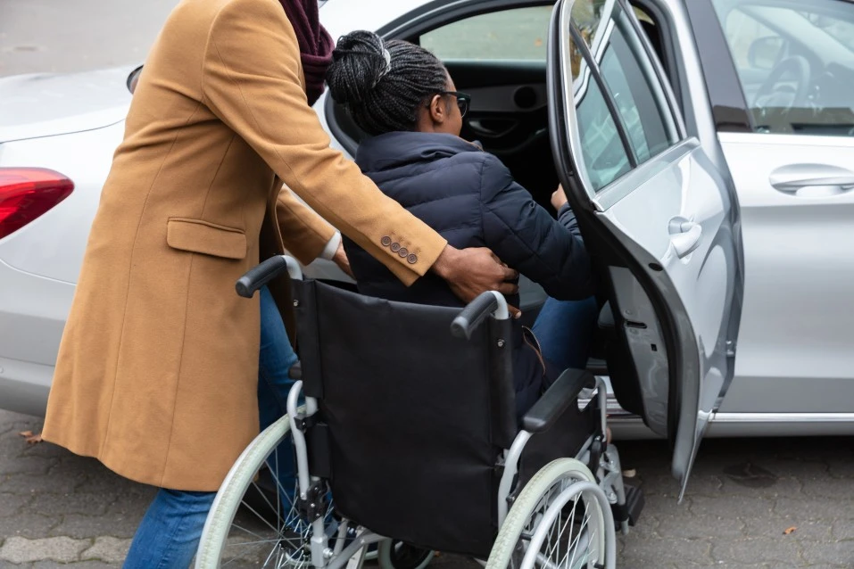 Disabled woman in wheelchair being helped into the car by support worker