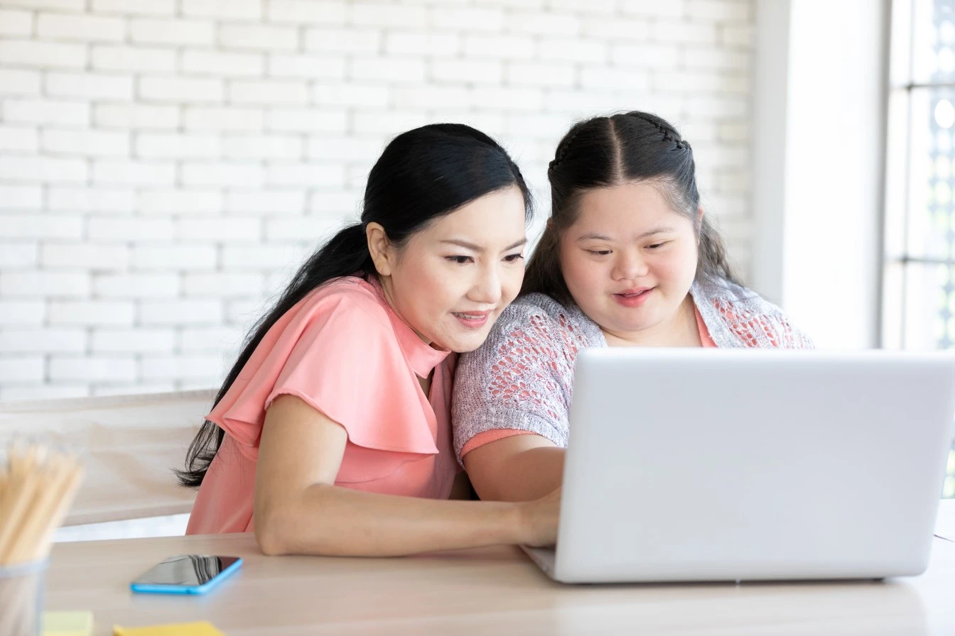 Disabled woman with down syndrome looking at laptop with support worker