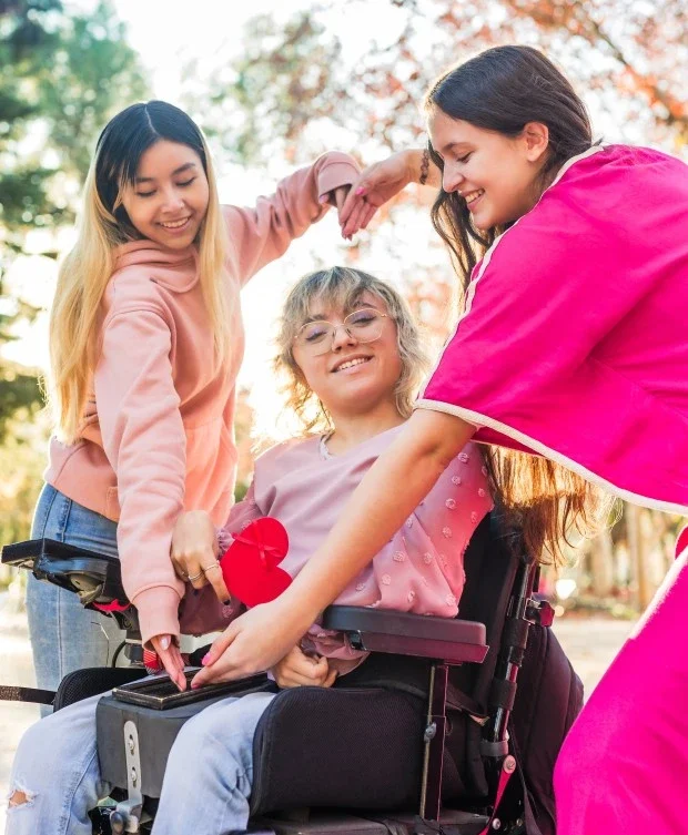 Happy disabled woman in wheelchair holding cut out love heart with two friends making love heart shape with arms