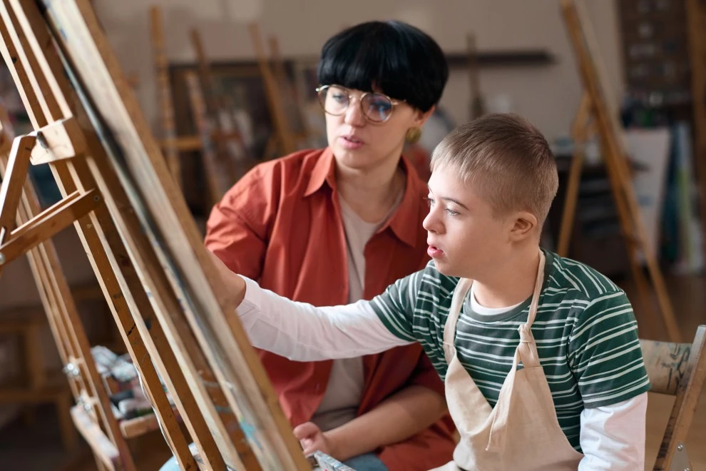 Disabled young man with down syndrome in art class with support worker